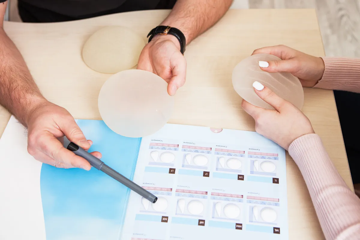 A breast surgeon and patient compare different breast implant samples during a consultation